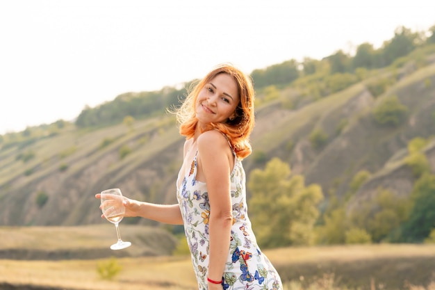 Beautiful red-haired girl is having fun and dancing in a field at sunset