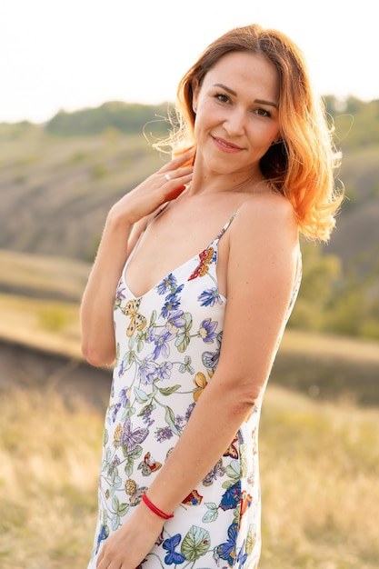 Beautiful red-haired girl is having fun and dancing in a field at sunset.