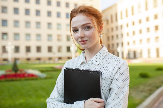 Beautiful red haired girl with freckles hugging notebooks 