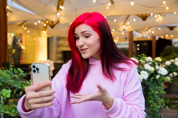 Beautiful red-haired influencer blogger girl in cafe talking making video call using smartphone with her subscribers in social networks.