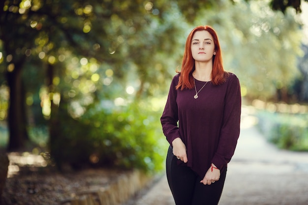 Beautiful red-haired young woman is walking in the autumn park. melancholy mood