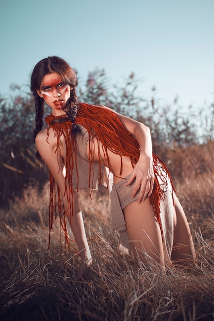 Beautiful red-skinned Indian woman kneels in the field and looks at the camera