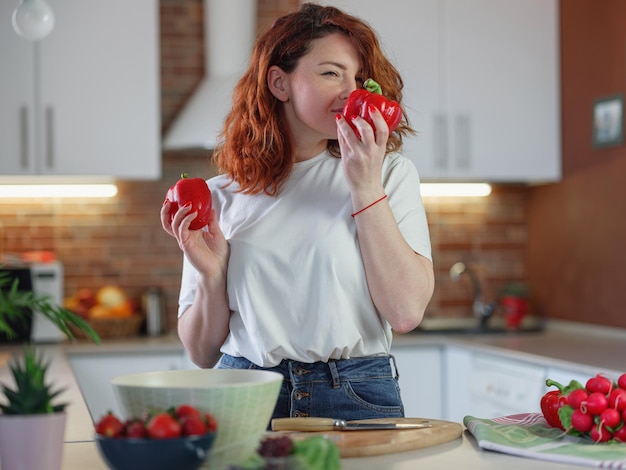 Beautiful redhair young woman is preparing vegetable salad in the kitchen