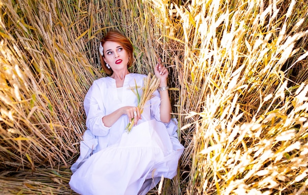 Beautiful redhead girl in a field of rye at sunset