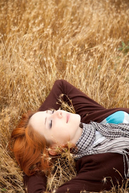 Beautiful redhead girl lying down on yellow grass. Autumn season time 