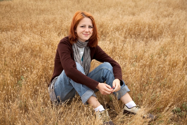 Beautiful redhead girl sitting on yellow grass. Autumn season time 