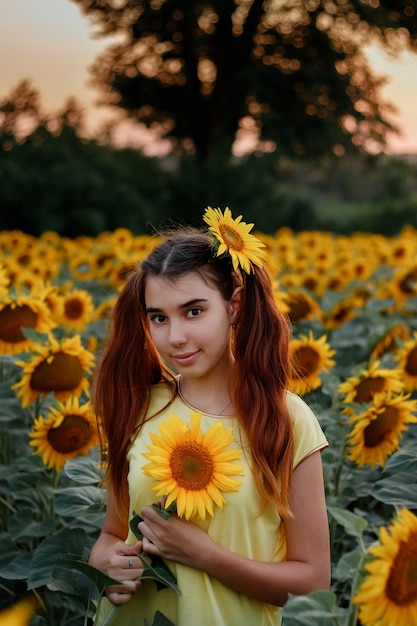 Beautiful redhead girl in a yellow tshirt on a field with sunflowers at sunset