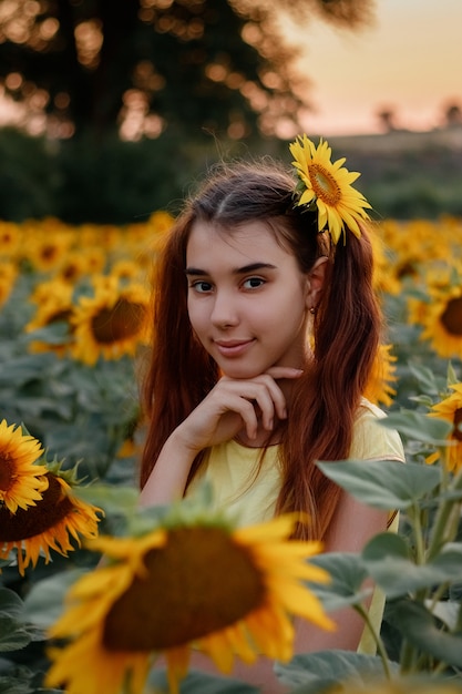 Beautiful redhead girl in a yellow tshirt on a field with sunflowers at sunset