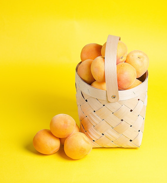 Beautiful and ripe apricots lie in a wooden basket on a yellow wall