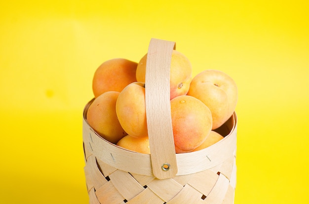 Beautiful and ripe apricots lie in a wooden basket on a yellow wall