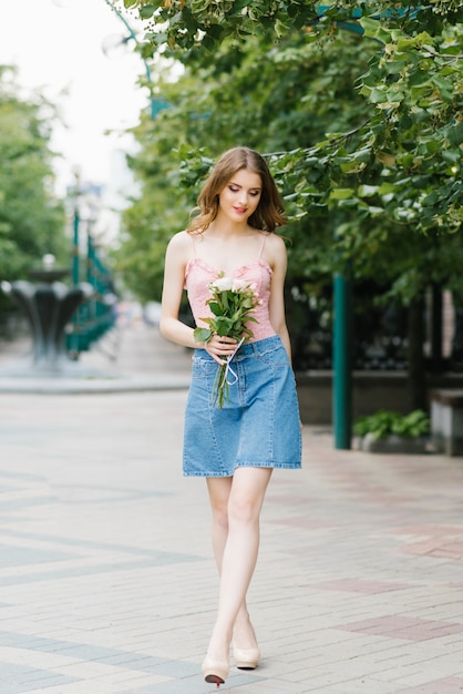 beautiful romantic young woman in a denim short skirt holds a bouquet of roses in her hands