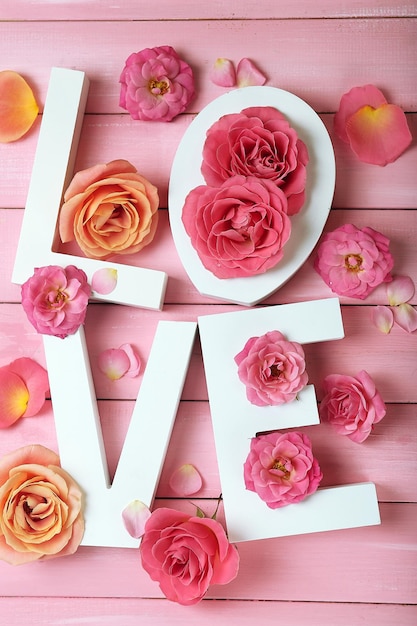 Beautiful roses with word LOVE on pink wooden planks background