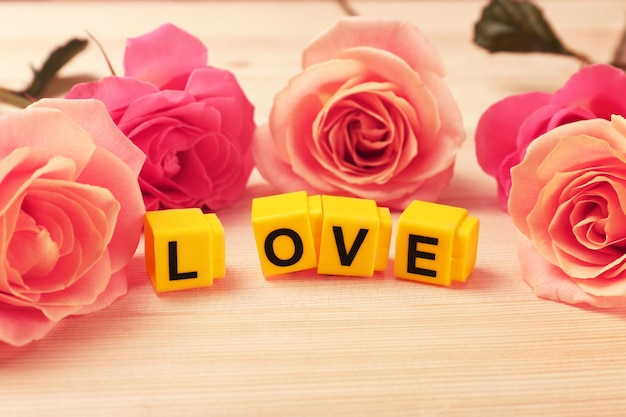 Beautiful roses with word LOVE on wooden background