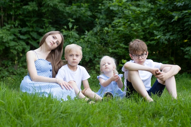 Beautiful sad woman with daughter and two sons resting on grass Young mother with three children sits on green lawn