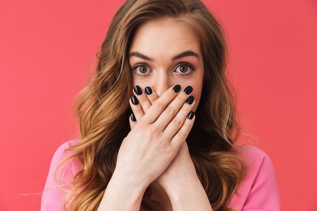 Beautiful scared young girl wearing casual clothes standing isolated over pink wall, cover mouth