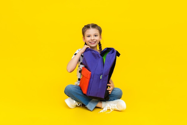 A beautiful schoolgirl on a yellow isolated background and looks at a new school backpack a child is going to extra classes after school an enhanced school program in high school