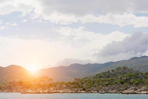 Beautiful seascape sun over the green mountains calm water and cloudy sky