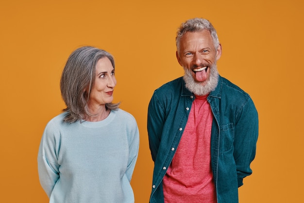 beautiful senior couple laughing while standing together against orange background