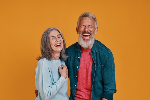 beautiful senior couple laughing while standing together against orange background