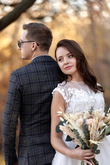 Beautiful sensual bride in white wedding dress and groom standing outdoor on natural background