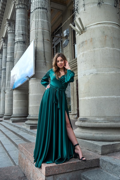 Beautiful sensual girl wearing long elegant green dress standing on the building steps. Relaxing Outside