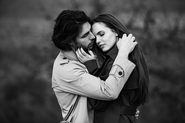 Beautiful sensual portrait of young stylish couple in love Image of adorable brunette couple in rain trench coat in park