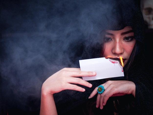 Beautiful serious mysterious woman in the darkness holding the burning tarot cards for the fortune teller read future