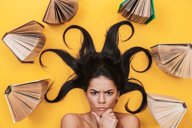 Photo beautiful serious young woman lies isolated on yellow wall over books