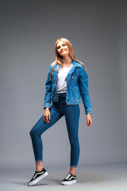 Photo beautiful sexy blonde woman dressed in a denim jacket and blue jeans fashion model in jeans clothing isolated on gray studio