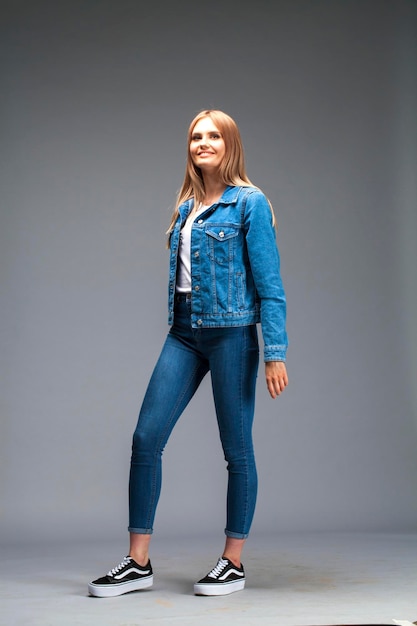 Photo beautiful sexy blonde woman dressed in a denim jacket and blue jeans fashion model in jeans clothing isolated on gray studio