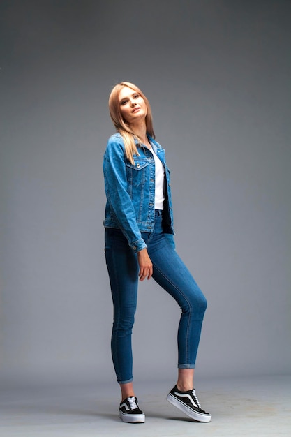 Beautiful sexy blonde woman dressed in a denim jacket and blue jeans Fashion model in jeans clothing Isolated on gray studio