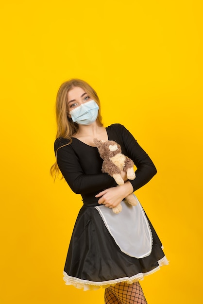 Beautiful sexy woman in maid clothes posing with rabbit toy  in covid protective mask