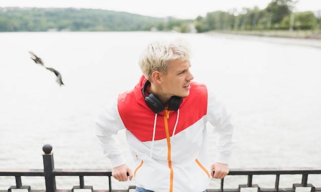 Beautiful shot of goodlooking attractive blond handsome man with headphones on neck walking and relax in the park of the city Street fashion style People lifestyle and technology concept