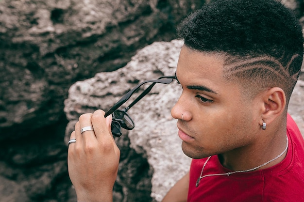 Beautiful shot of a young man taking his sunglasses off  while sitting on the rocks near the lake