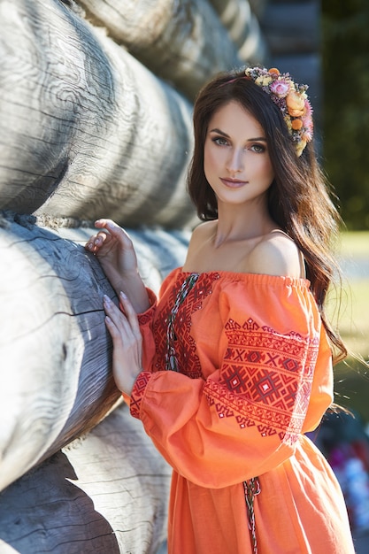 Beautiful Slavic woman in an orange ethnic dress and a wreath of flowers on her head