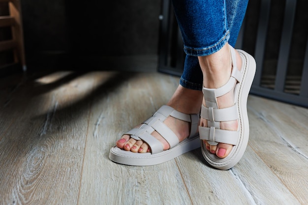 Beautiful slender female legs in leather sandals on the floor against gray parquet Collection of women's sandals