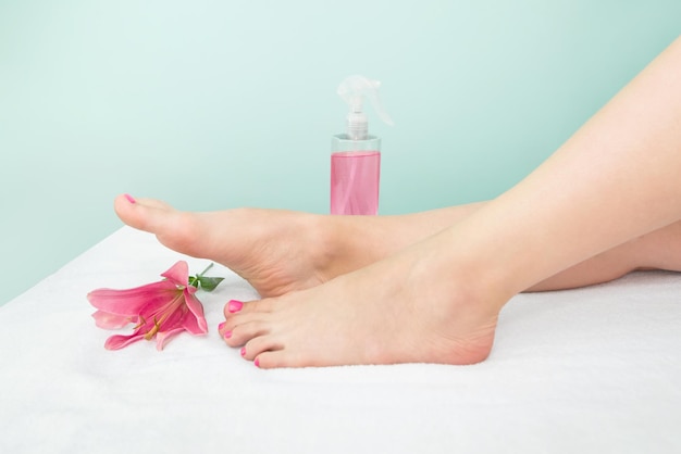 Beautiful slender female legs spray bottle with pink liquid and rose flower The concept of cosmetology shugaring Cropped photo of female legs