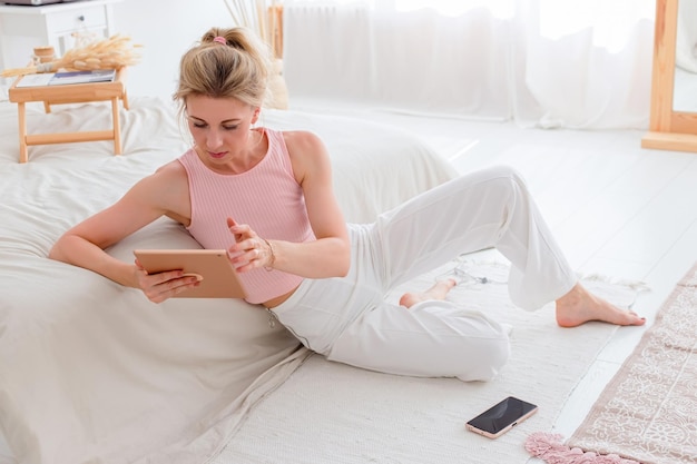 A beautiful slender woman sits on the floor in the morning watches a digital tablet