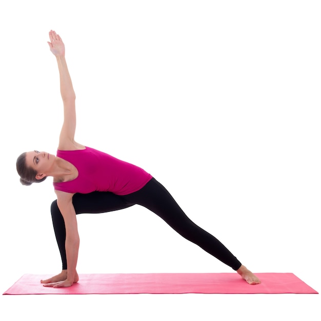 Beautiful slim sporty woman standing on pink mat in yoga pose isolated on white background