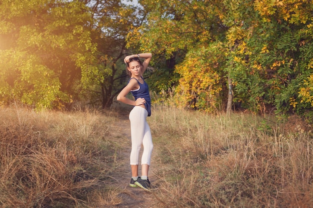 Beautiful slim sporty woman standing at sunset in the field in autumn. Lifestyle background