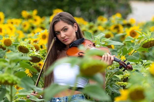 Beautiful slim teenager woman with violin in yellow blooming sunflower field