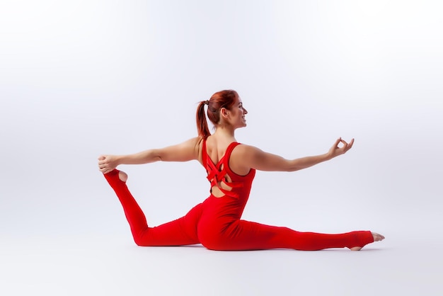 Beautiful slim woman in sports overalls doing yoga standing in an asana balancing pose on white isolated background The concept of sports and meditation Training for stretching and yoga