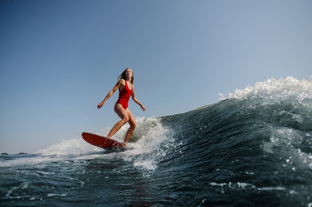 Beautiful slim woman surfing on a high blue wave