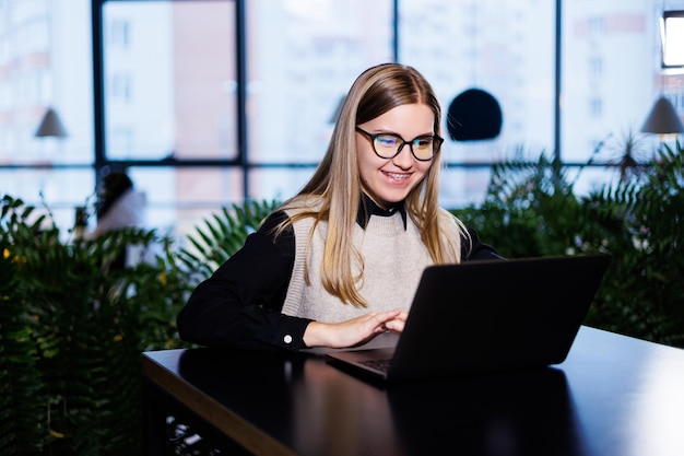 Beautiful smart attractive elegant woman businesswoman in a large company holds an online meeting with international business partners, she sits at a table at the workplace with a laptop