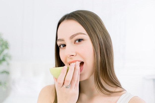 Beautiful smile, white strong teeth. Head and shoulders of young woman with snow-white smile holding green apple, teethcare.