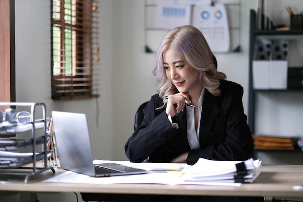 Beautiful smiling Asian businesswoman hand holding pen working using tablet at office