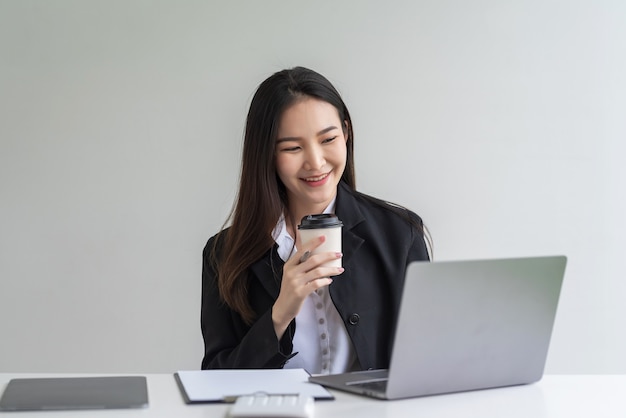 Beautiful smiling Asian businesswoman happy success holding a coffee cup tablet placed at the office.