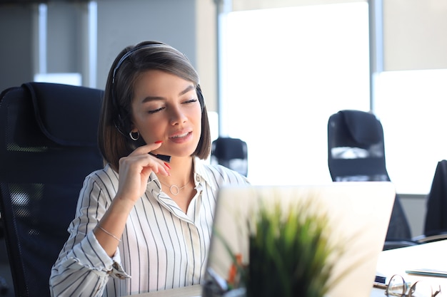 Beautiful smiling call center worker in headphones is working at modern office.