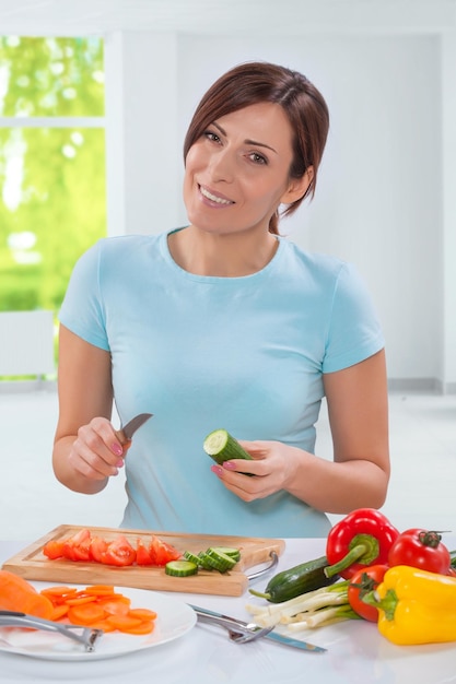 Beautiful smiling caucasian model holding cucumber with kitchen knife and looking at camera