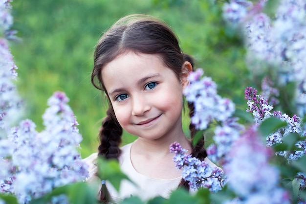 Beautiful smiling child girl in the pink dress on field of red clover in sunset time.